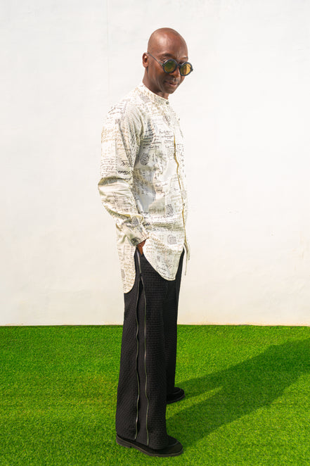 Linen Digital Shirt featuring a cream long-line tunic with black script patterns, a mandarin collar, and side slits paired with black textured wide-leg trousers.