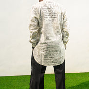 Linen Digital Shirt featuring a cream long-line tunic with black script patterns, a mandarin collar, and side slits paired with black textured wide-leg trousers. Back view.