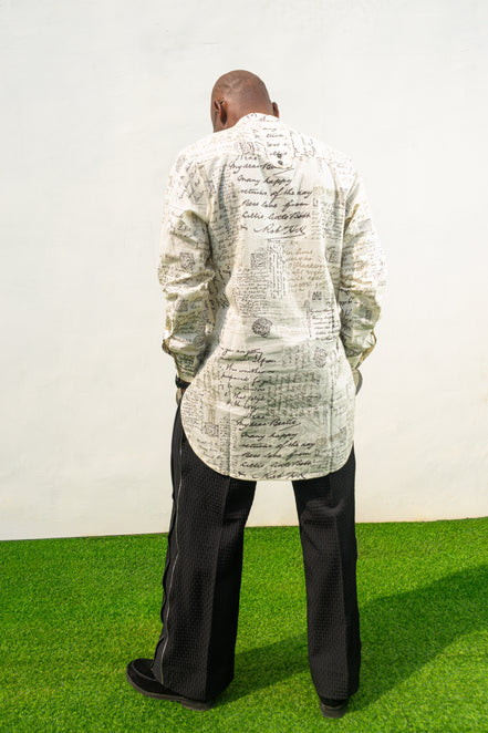 Linen Digital Shirt featuring a cream long-line tunic with black script patterns, a mandarin collar, and side slits paired with black textured wide-leg trousers. Back view.