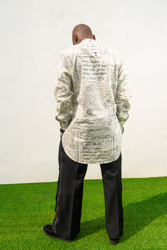 Linen Digital Shirt featuring a cream long-line tunic with black script patterns, a mandarin collar, and side slits paired with black textured wide-leg trousers. Back view.