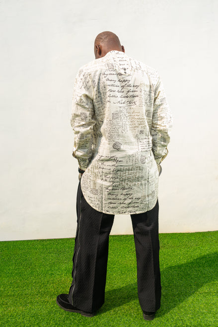 Linen Digital Shirt featuring a cream long-line tunic with black script patterns, a mandarin collar, and side slits paired with black textured wide-leg trousers. Back view.