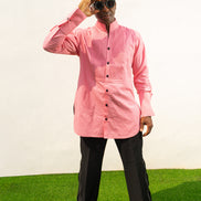 Long Sleeve Shirt featuring a vibrant pink textured fabric, a pleated tuxedo-style chest plate, dark contrast buttons, and a structured mandarin neckline. 