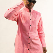 Long Sleeve Shirt featuring a vibrant pink textured fabric, a pleated tuxedo-style chest plate, dark contrast buttons, and a structured mandarin neckline. 