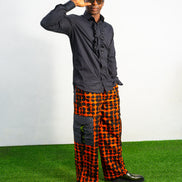 Modern African clothing for men, specifically wide-leg, geometric-patterned Ankara cargo pants in black and orange.