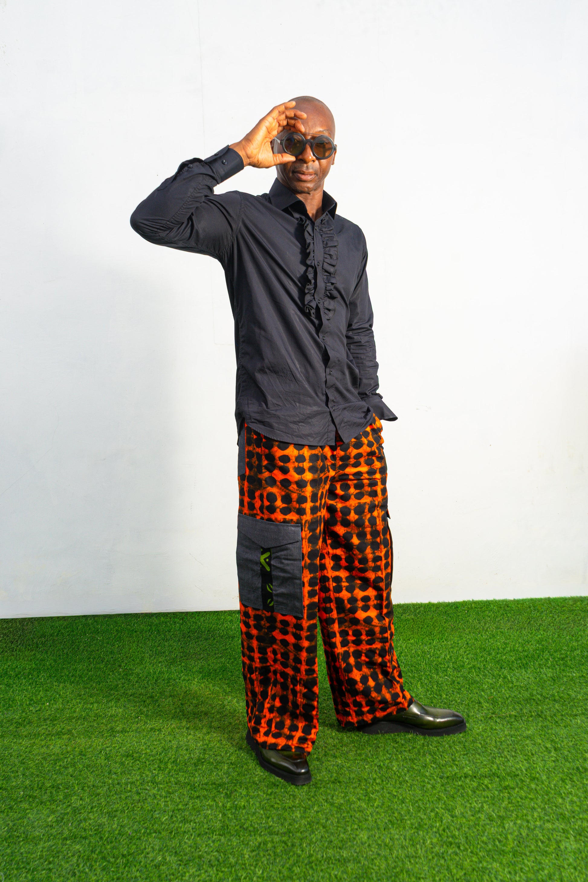 Modern African clothing for men, specifically wide-leg, geometric-patterned Ankara cargo pants in black and orange.