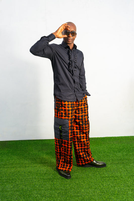 Modern African clothing for men, specifically wide-leg, geometric-patterned Ankara cargo pants in black and orange.