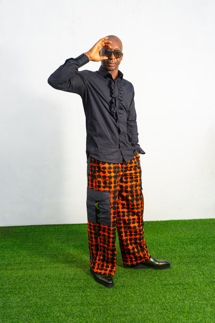 Modern African clothing for men, specifically wide-leg, geometric-patterned Ankara cargo pants in black and orange.