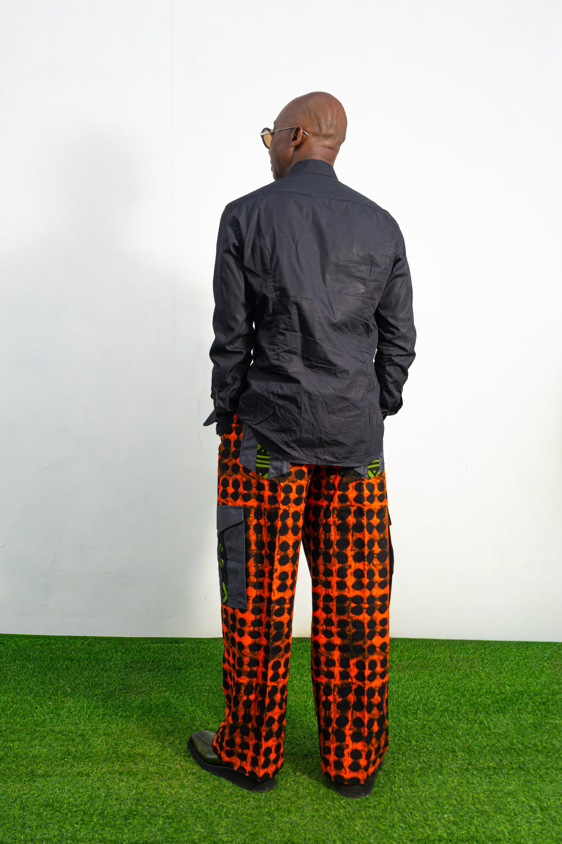Modern African clothing for men, specifically wide-leg, geometric-patterned Ankara cargo pants in black and orange.