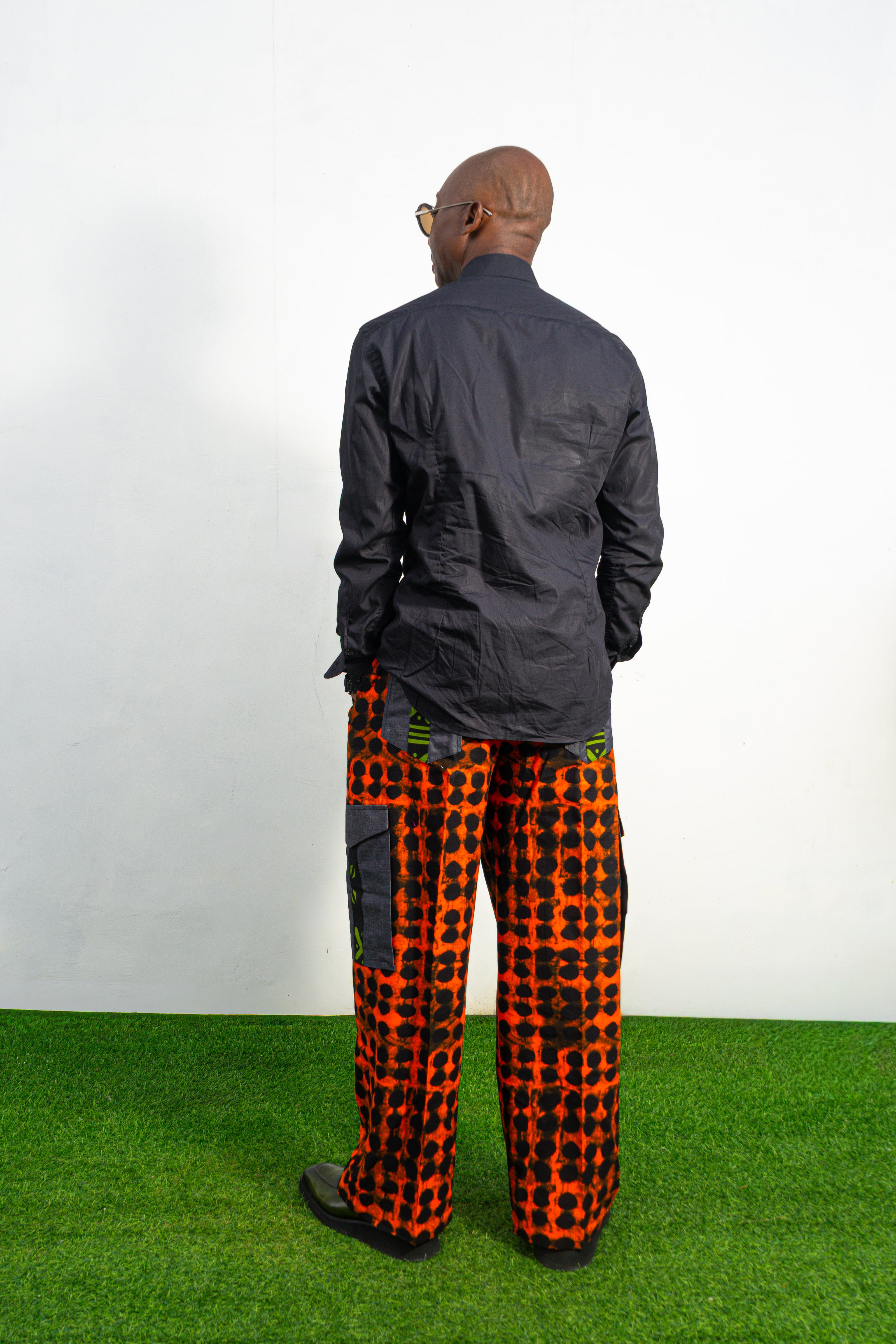 Modern African clothing for men, specifically wide-leg, geometric-patterned Ankara cargo pants in black and orange.