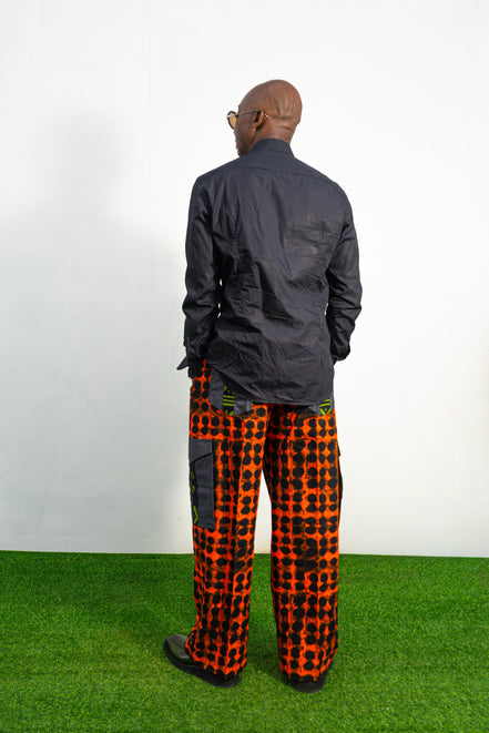 Modern African clothing for men, specifically wide-leg, geometric-patterned Ankara cargo pants in black and orange.