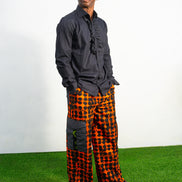Modern African clothing for men, specifically wide-leg, geometric-patterned Ankara cargo pants in black and orange.
