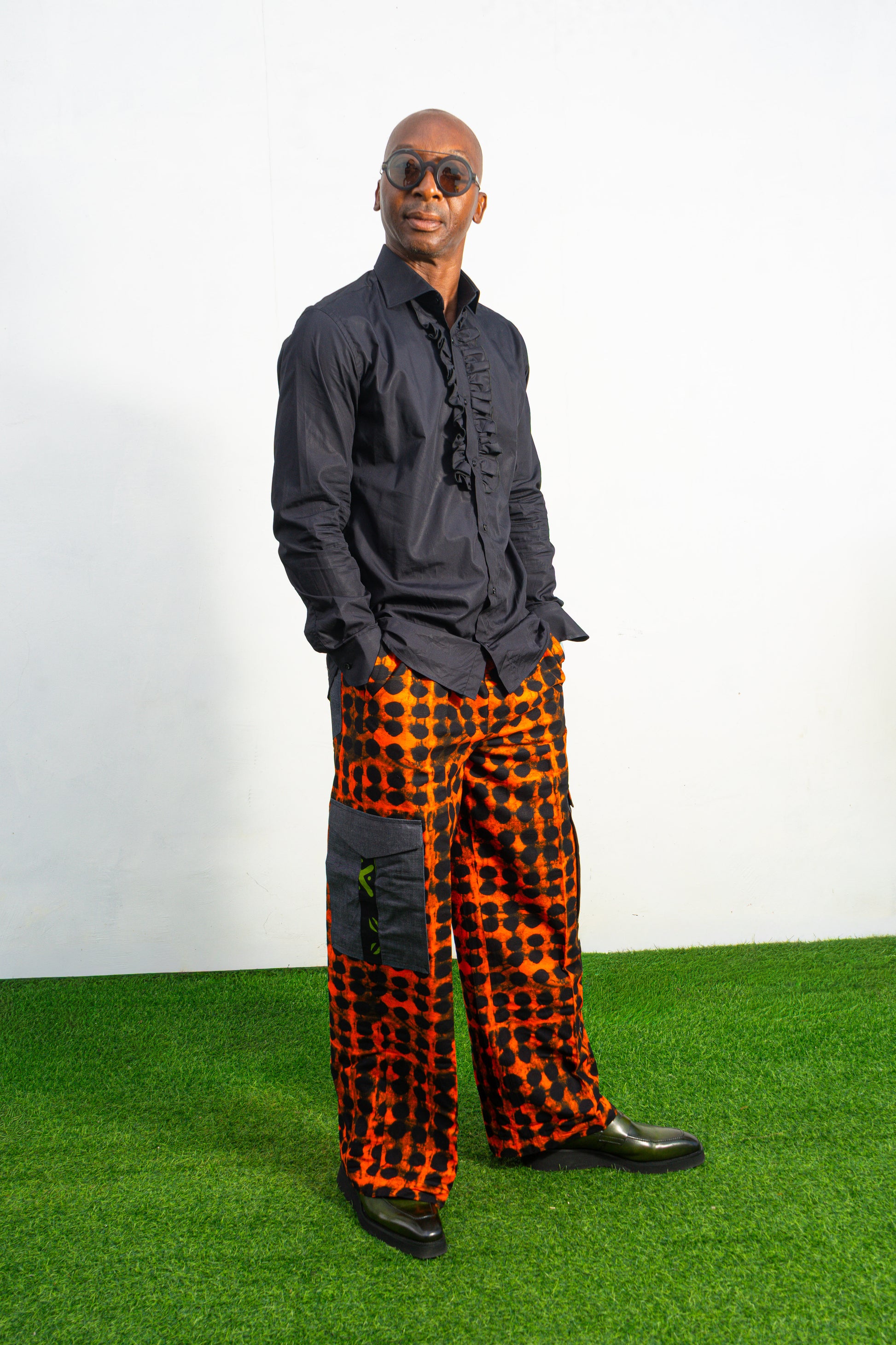 Modern African clothing for men, specifically wide-leg, geometric-patterned Ankara cargo pants in black and orange.