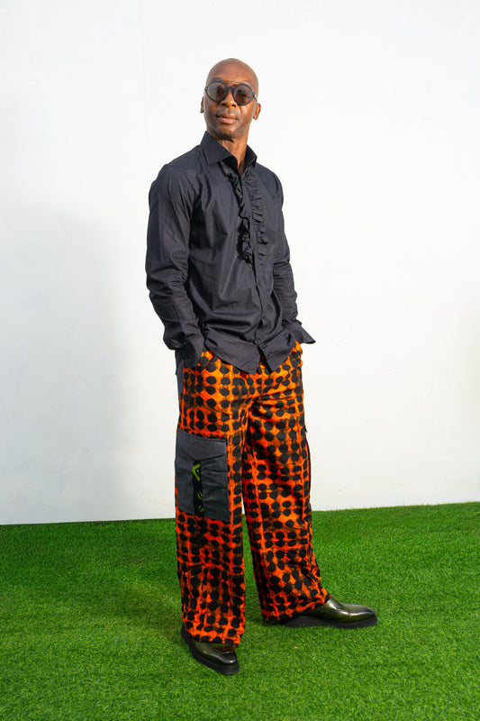 Modern African clothing for men, specifically wide-leg, geometric-patterned Ankara cargo pants in black and orange.