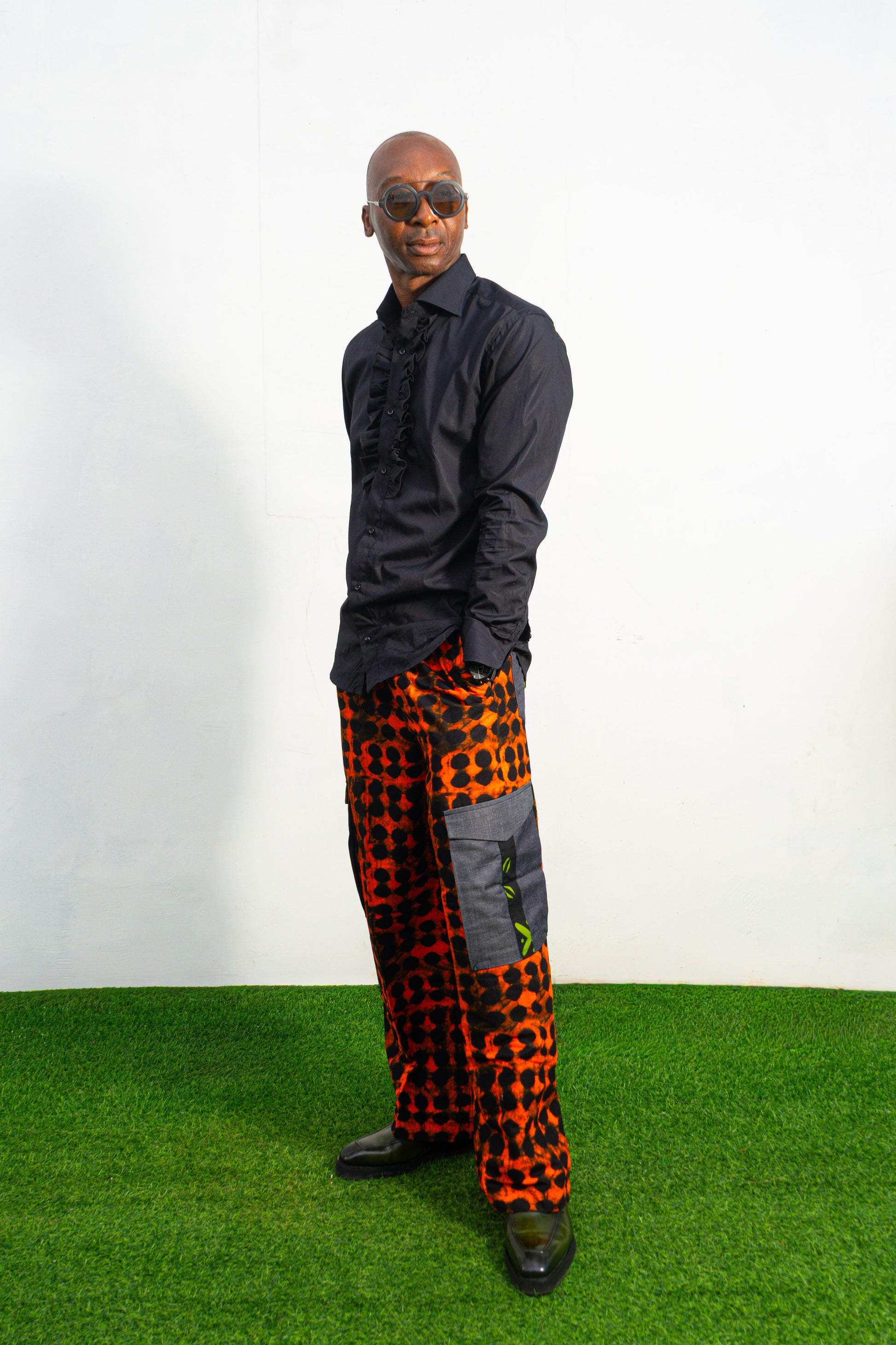 Modern African clothing for men, specifically wide-leg, geometric-patterned Ankara cargo pants in black and orange.