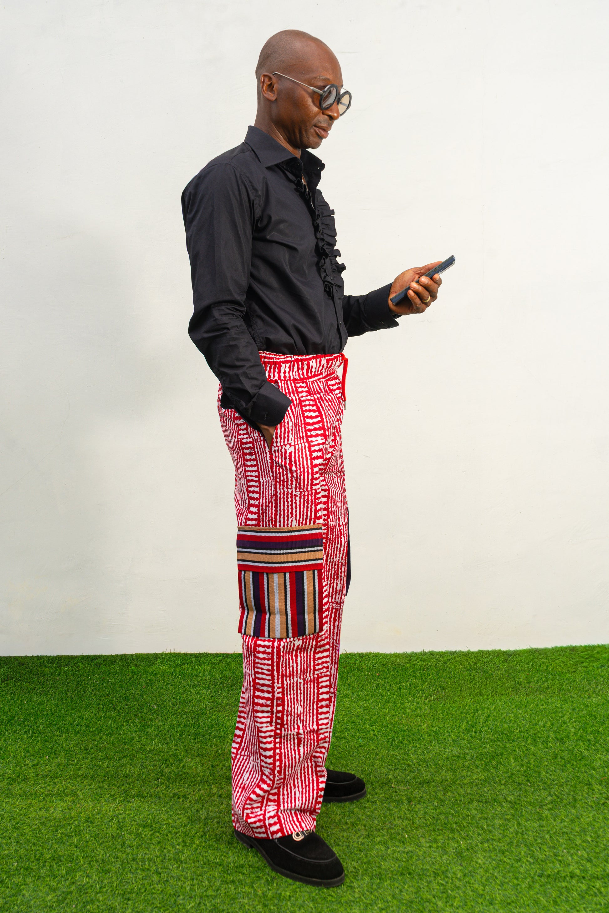Men's cargo pants featuring a red and white Ankara print, a straight-leg silhouette, and multi-colored striped pocket details.