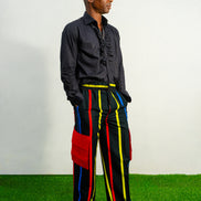 Men's wide-leg cargo pants featuring a black background with vertical red, yellow, and blue stripes and large red side pockets.