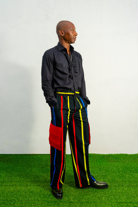 Men's wide-leg cargo pants featuring a black background with vertical red, yellow, and blue stripes and large red side pockets.