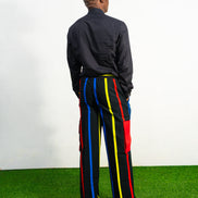 Men's wide-leg cargo pants featuring a black background with vertical red, yellow, and blue stripes and large red side pockets.