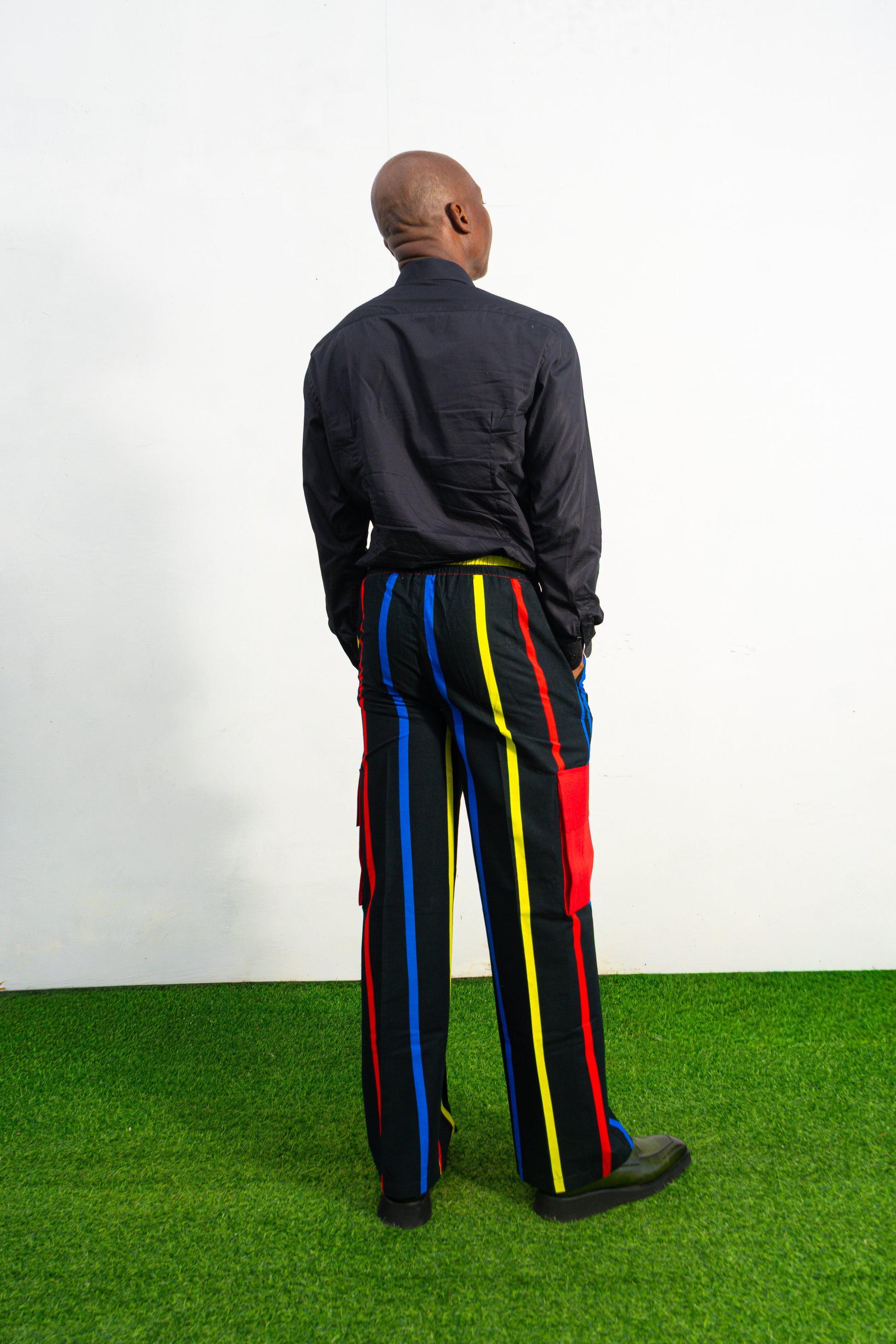 Men's wide-leg cargo pants featuring a black background with vertical red, yellow, and blue stripes and large red side pockets.
