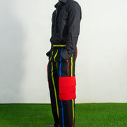 Men's wide-leg cargo pants featuring a black background with vertical red, yellow, and blue stripes and large red side pockets.