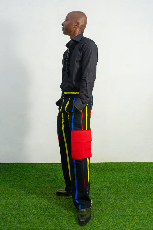 Men's wide-leg cargo pants featuring a black background with vertical red, yellow, and blue stripes and large red side pockets.