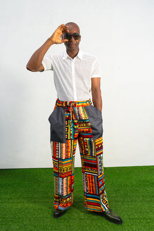 Men's wide-leg pants featuring a vibrant multicolored Ankara patchwork print and oversized grey side pockets.
