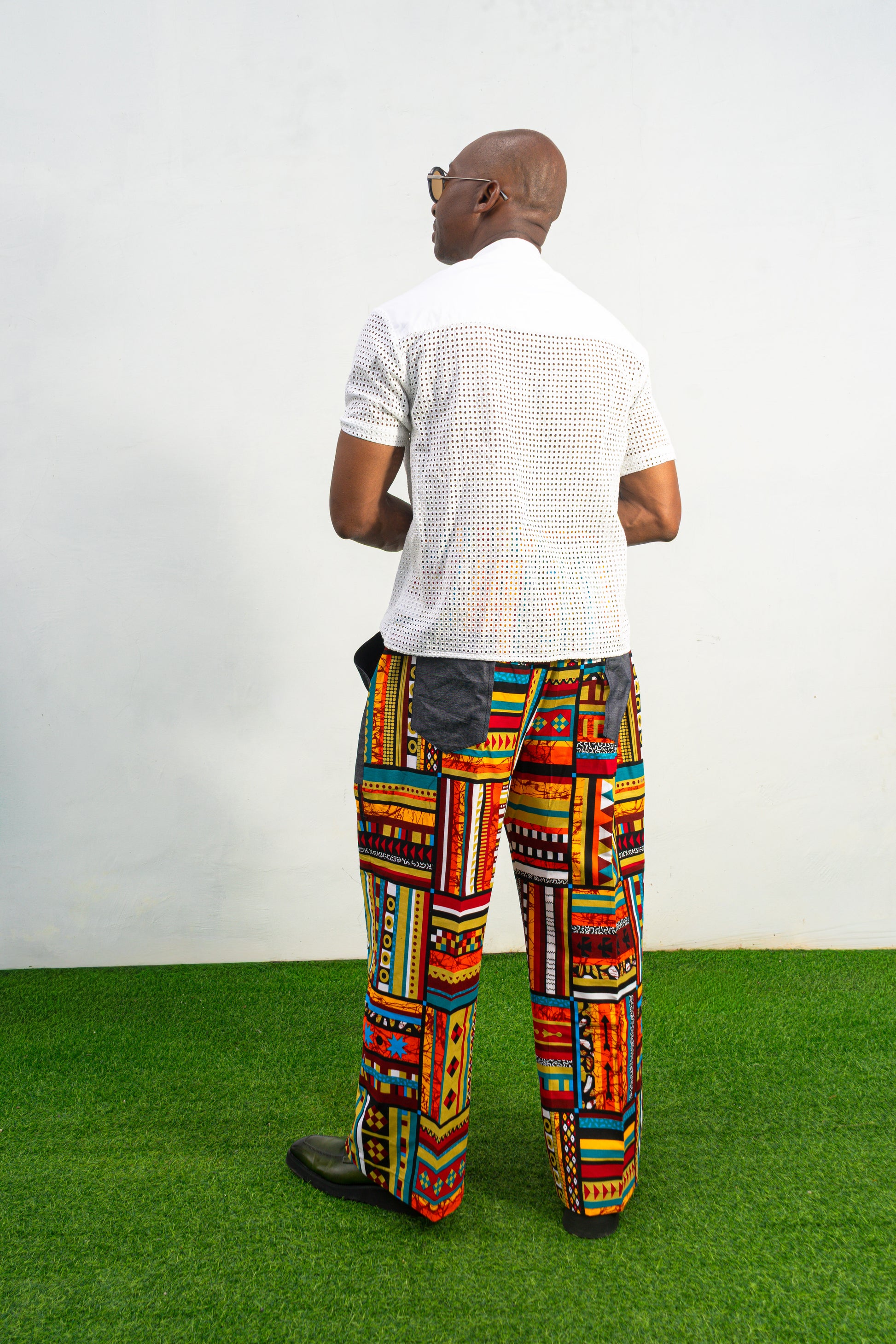 Men's wide-leg pants featuring a vibrant multicolored Ankara patchwork print and oversized grey side pockets.