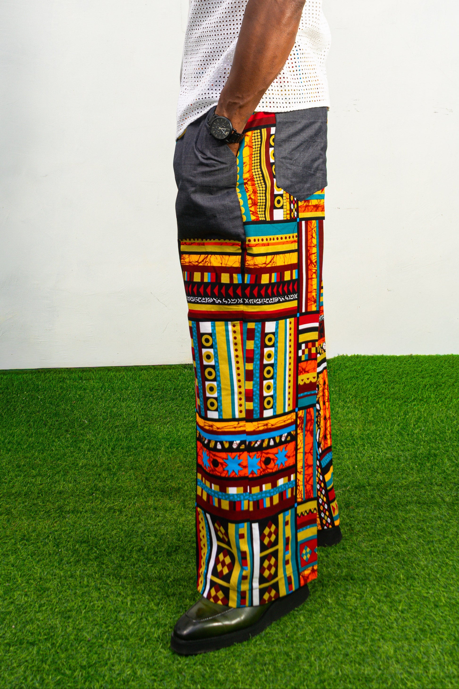 Men's wide-leg pants featuring a vibrant multicolored Ankara patchwork print and oversized grey side pockets.
