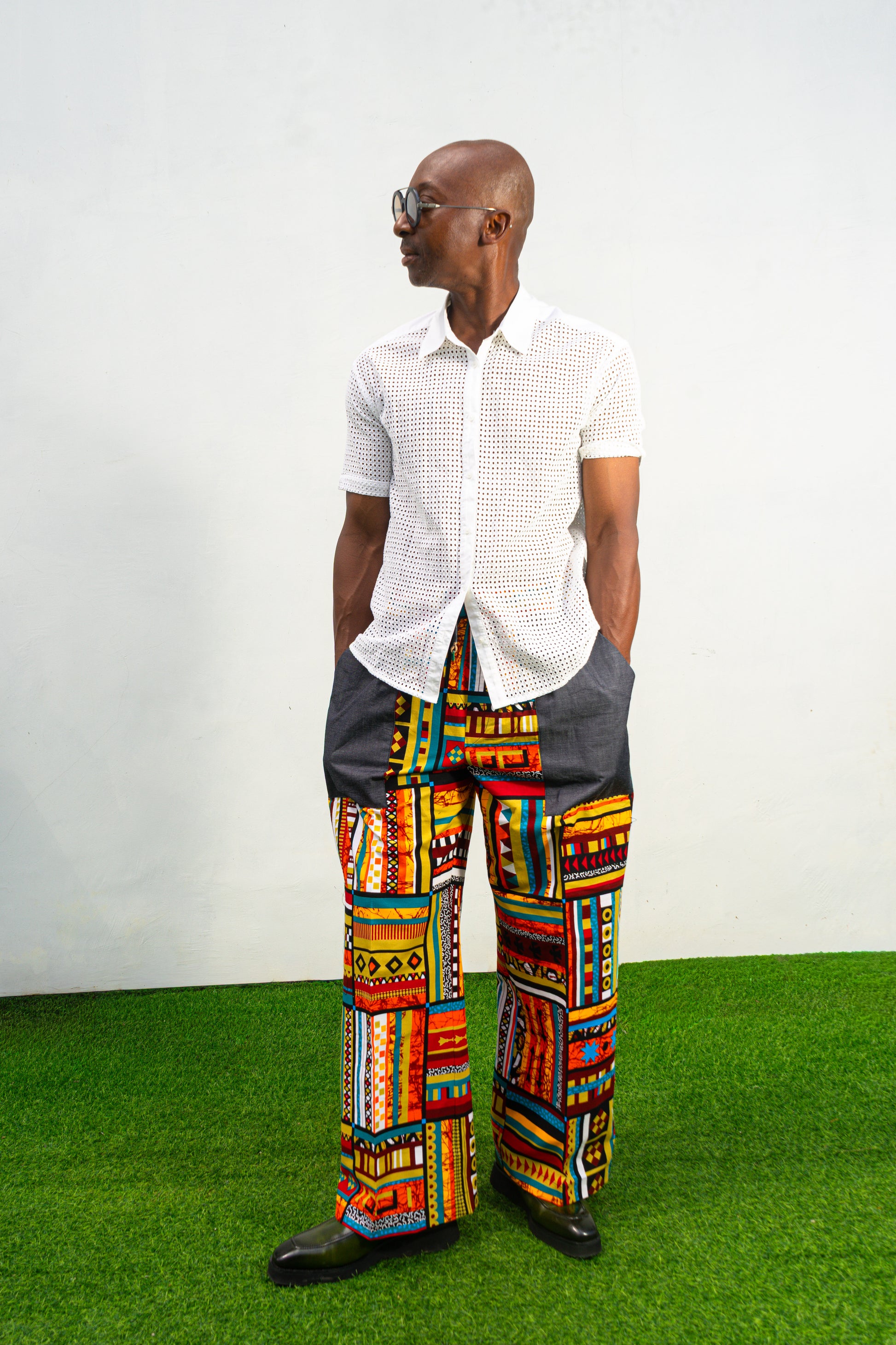 Men's wide-leg pants featuring a vibrant multicolored Ankara patchwork print and oversized grey side pockets.