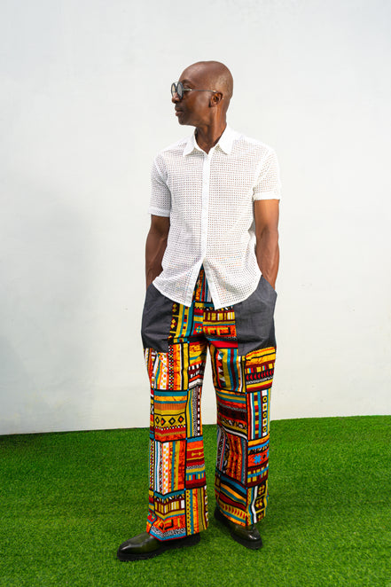 Men's wide-leg pants featuring a vibrant multicolored Ankara patchwork print and oversized grey side pockets.