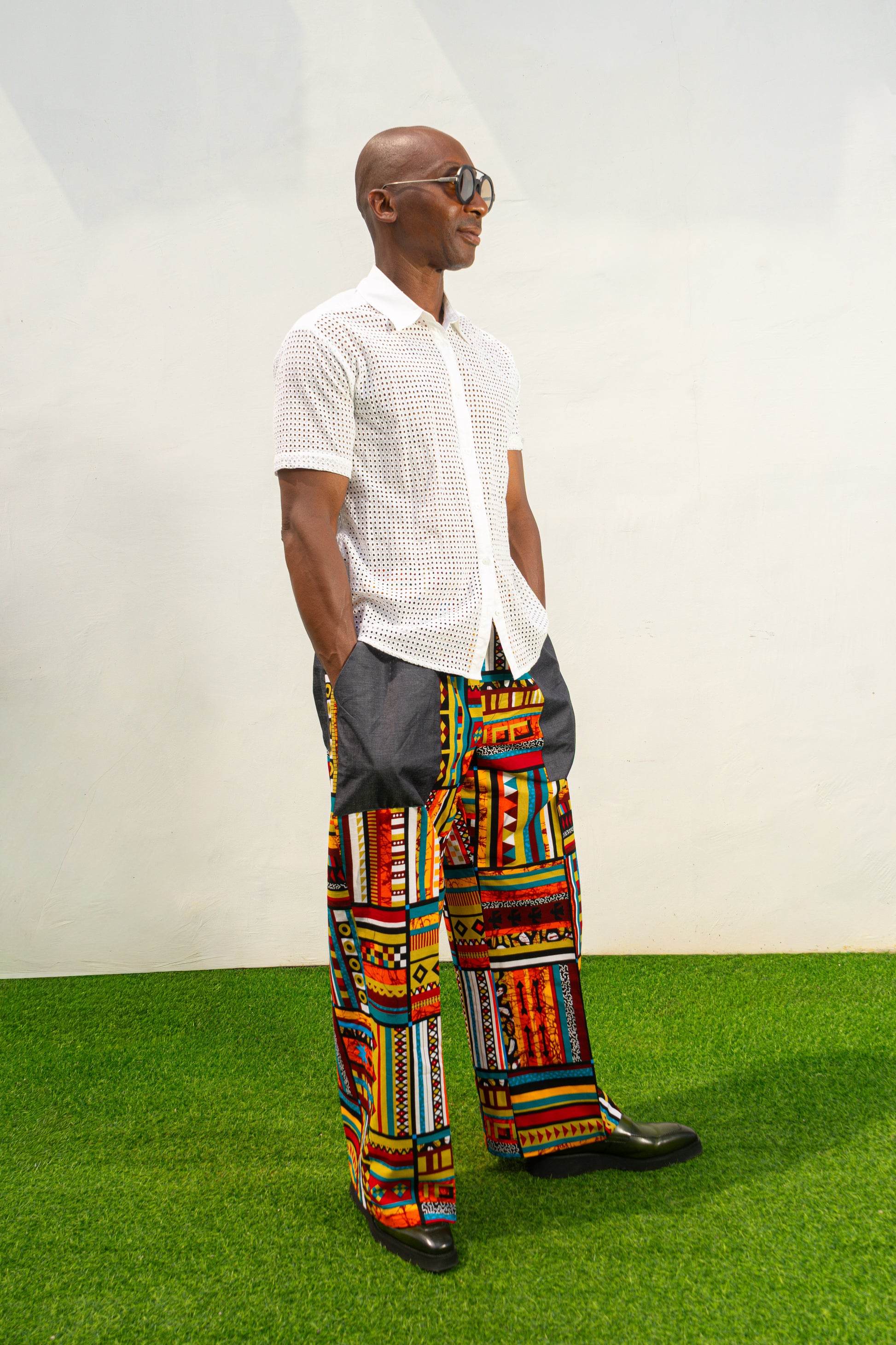 Men's wide-leg pants featuring a vibrant multicolored Ankara patchwork print and oversized grey side pockets.