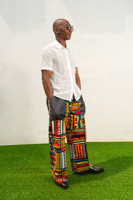 Men's wide-leg pants featuring a vibrant multicolored Ankara patchwork print and oversized grey side pockets.