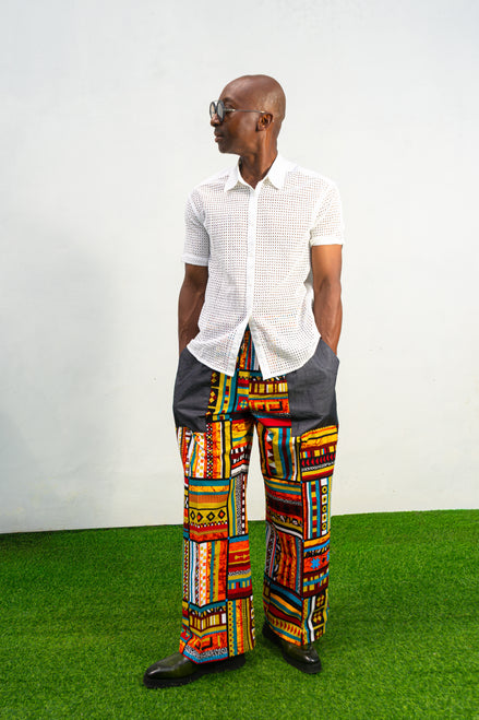 Men's wide-leg pants featuring a vibrant multicolored Ankara patchwork print and oversized grey side pockets.