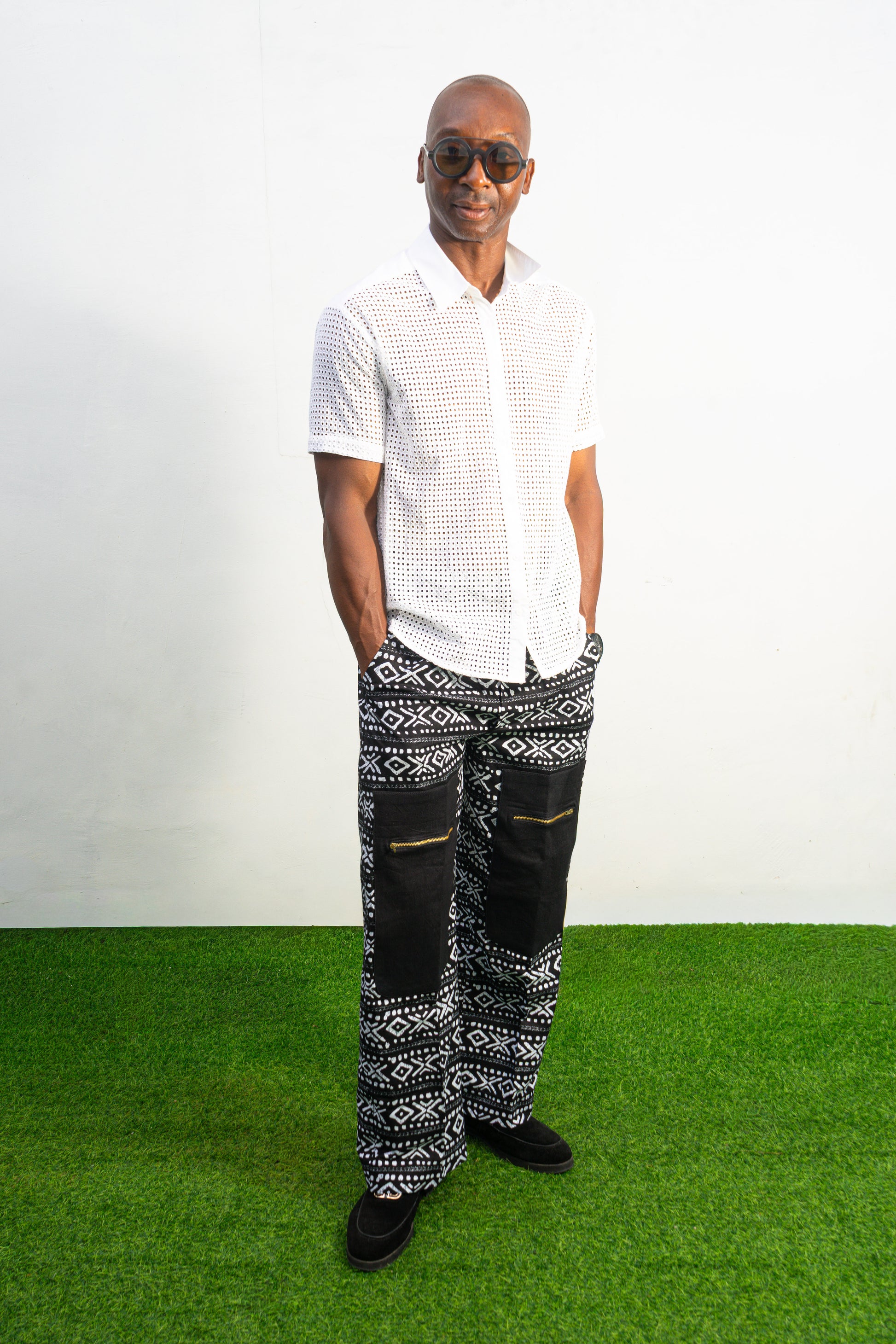 Mens pants featuring a black and white geometric Ankara print with large black front pockets, gold zippers, and a relaxed wide-leg cut.