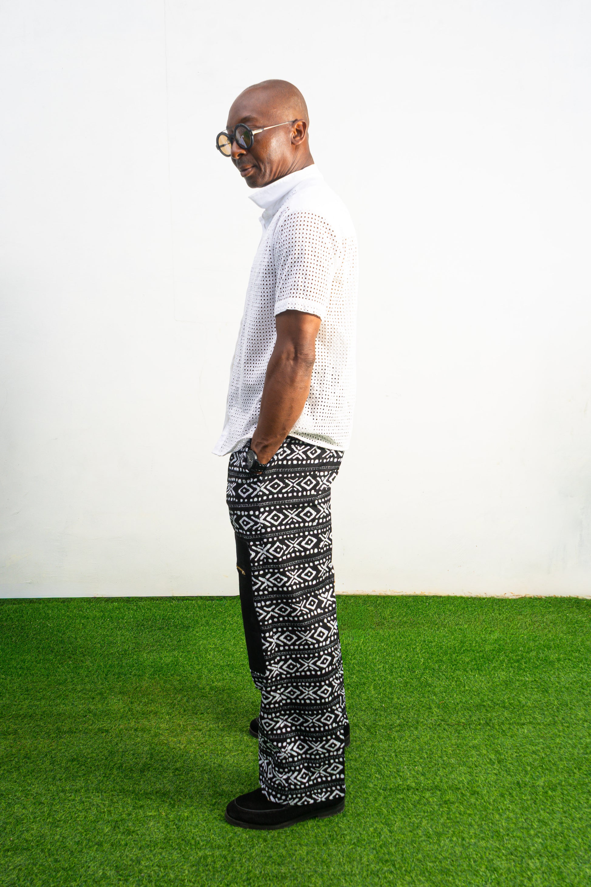 Mens pants featuring a black and white geometric Ankara print with large black front pockets, gold zippers, and a relaxed wide-leg cut.