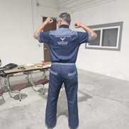 Modern Jumpsuit featuring a deep blue denim fabrication, light-wash contrast trim details on the short sleeves, back yoke, and curved utility pockets, complete with a structured mandarin collar and a front zip closure.