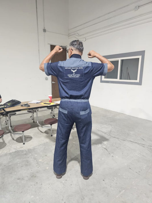 Modern Jumpsuit featuring a deep blue denim fabrication, light-wash contrast trim details on the short sleeves, back yoke, and curved utility pockets, complete with a structured mandarin collar and a front zip closure.