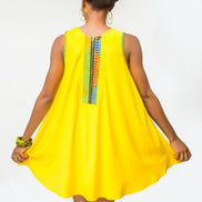 Shift Dress featuring a sleeveless, flowing yellow jersey mini dress accented with colorful geometric African print accents at the shoulders and large curved side patch pockets