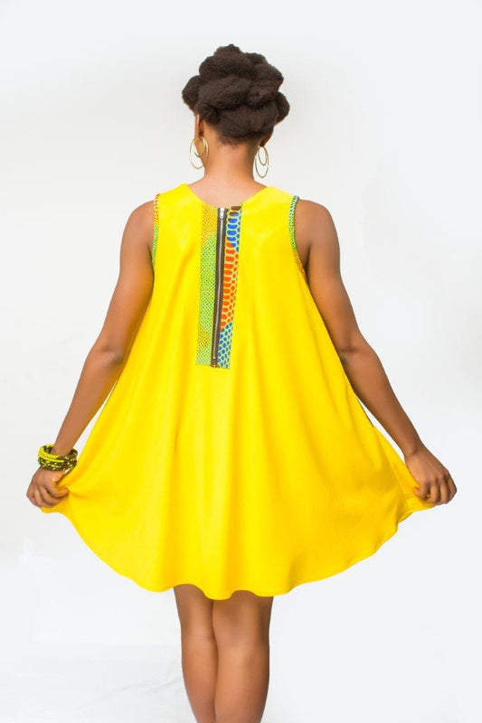 Shift Dress featuring a sleeveless, flowing yellow jersey mini dress accented with colorful geometric African print accents at the shoulders and large curved side patch pockets