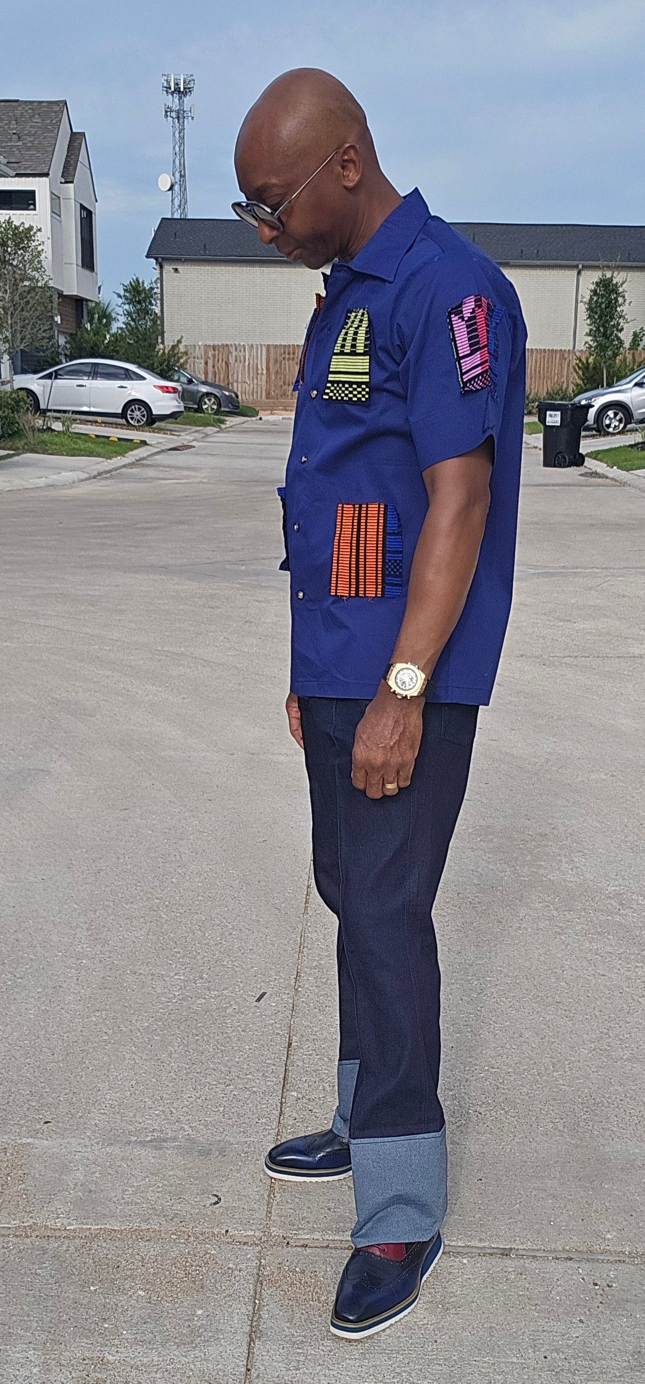 Shirt featuring a short-sleeved royal blue button-down design with vibrant geometric African print patches on the chest, sleeves, and front waist.