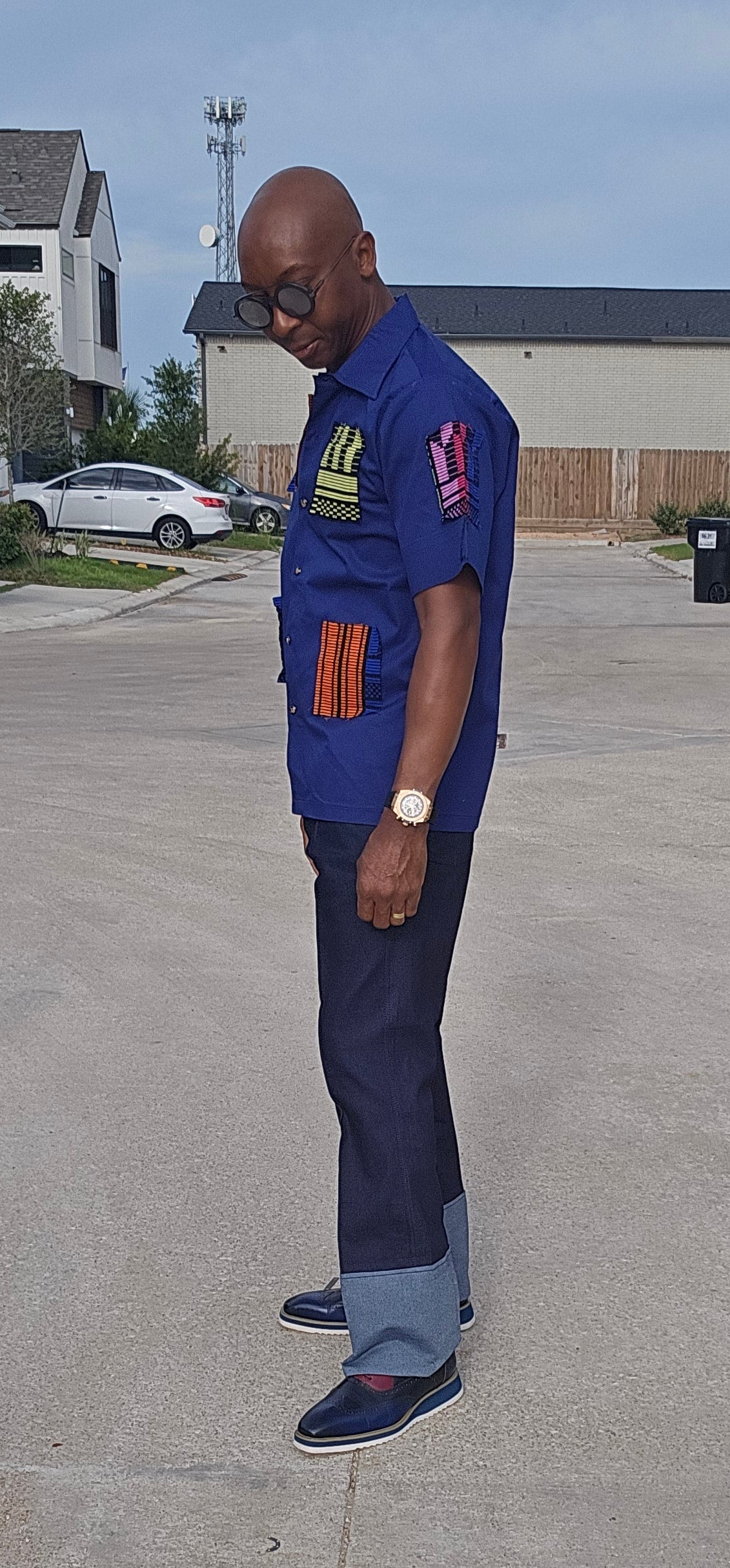 Shirt featuring a short-sleeved royal blue button-down design with vibrant geometric African print patches on the chest, sleeves, and front waist.