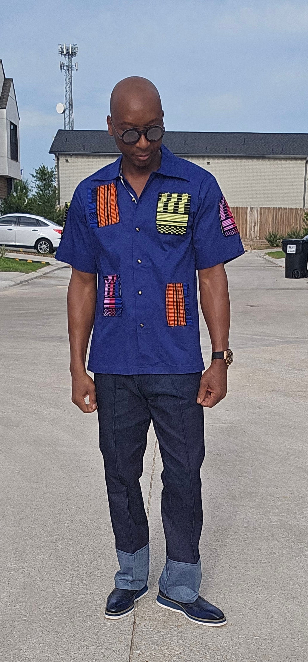 Shirt featuring a short-sleeved royal blue button-down design with vibrant geometric African print patches on the chest, sleeves, and front waist.