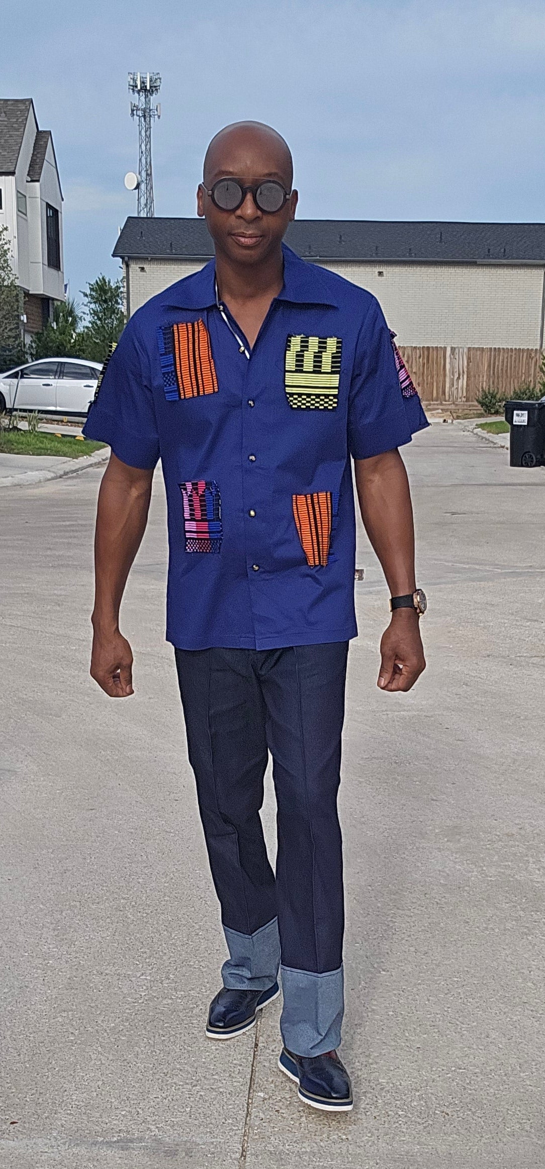 Shirt featuring a short-sleeved royal blue button-down design with vibrant geometric African print patches on the chest, sleeves, and front waist.