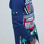 Shirt featuring an abstract geometric front panel in bright pink, teal, blue, and black-and-white lines, finished with navy blue sleeves that display three horizontal pleated cutouts.