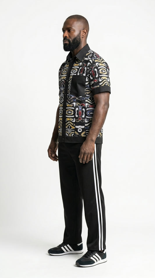 Shirt featuring a short-sleeved button-down silhouette dominated by an abstract, geometric Ankara pattern in white, yellow, and red tones, framed by a solid black collar, pocket, placket, and sleeve bands.