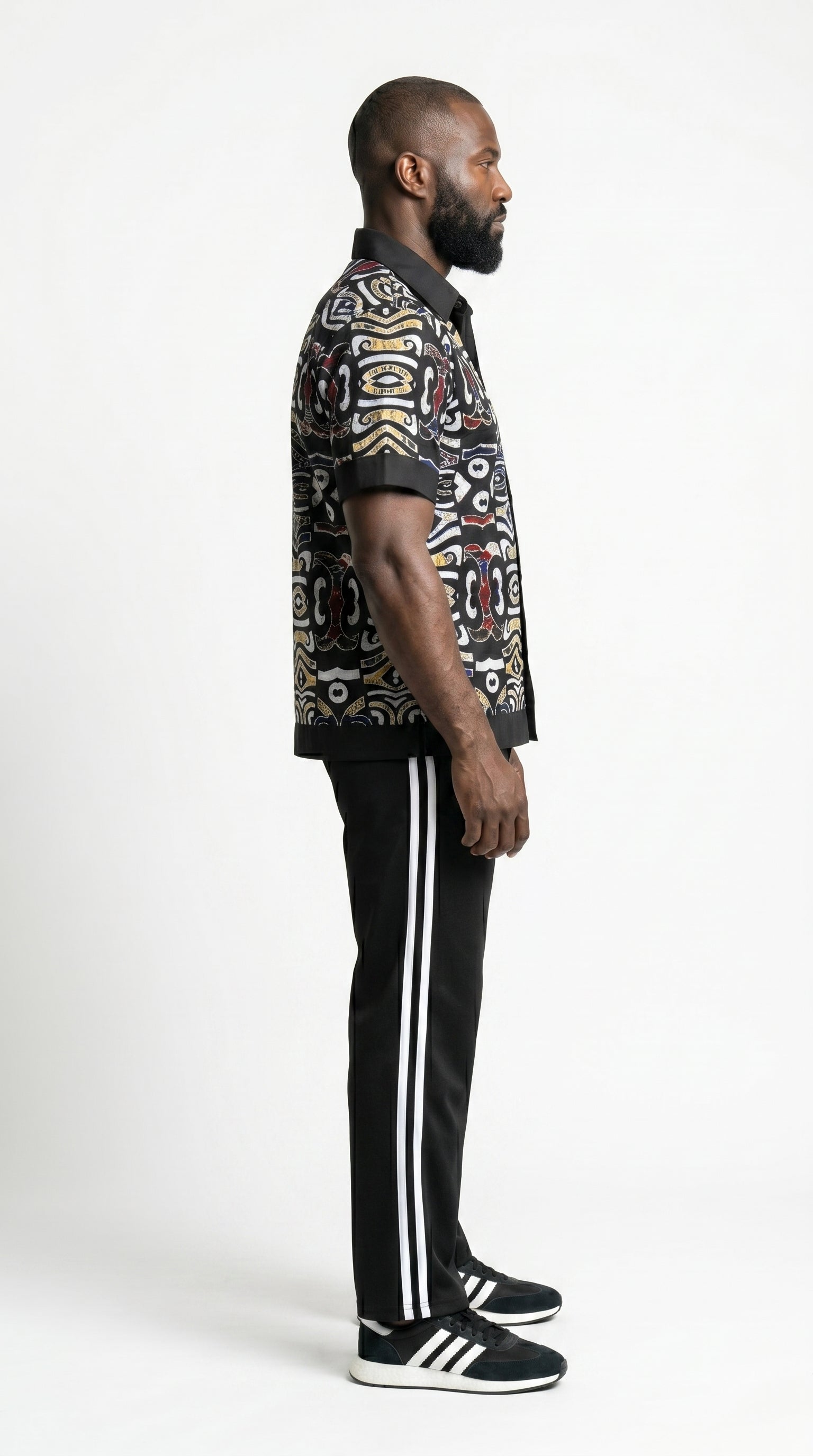 Shirt featuring a short-sleeved button-down silhouette dominated by an abstract, geometric Ankara pattern in white, yellow, and red tones, framed by a solid black collar, pocket, placket, and sleeve bands.
