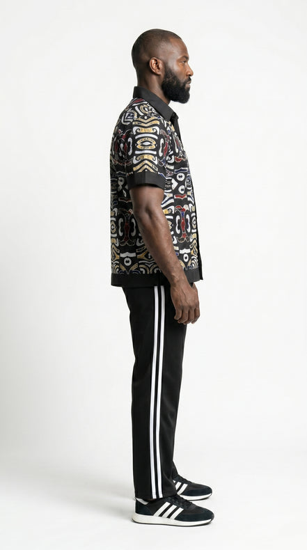 Shirt featuring a short-sleeved button-down silhouette dominated by an abstract, geometric Ankara pattern in white, yellow, and red tones, framed by a solid black collar, pocket, placket, and sleeve bands.
