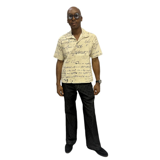 Short-sleeve cotton shirt featuring a black cursive script pattern on a cream-colored fabric with a button-down front and camp collar.