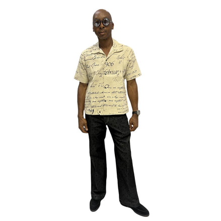 Short-sleeve cotton shirt featuring a black cursive script pattern on a cream-colored fabric with a button-down front and camp collar.