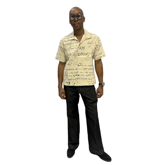Short-sleeve cotton shirt featuring a black cursive script pattern on a cream-colored fabric with a button-down front and camp collar.